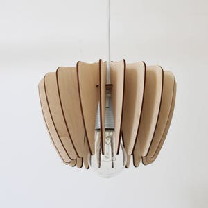 May include: A wooden pendant light fixture with a unique, geometric design. The light fixture is made of thin, overlapping wooden slats that create a fan-like shape. The light fixture is suspended from a white cord.