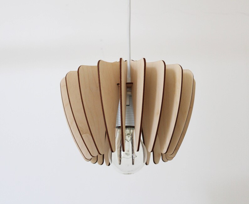 May include: A wooden pendant light fixture with a unique, geometric design. The light fixture is made of thin, overlapping wooden slats that create a fan-like shape. The light fixture is suspended from a white cord.