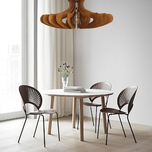May include: A wooden dining table with four chairs. The table is round and has a light wood finish. The chairs are black metal with a brown woven seat. A wooden pendant light hangs above the table.