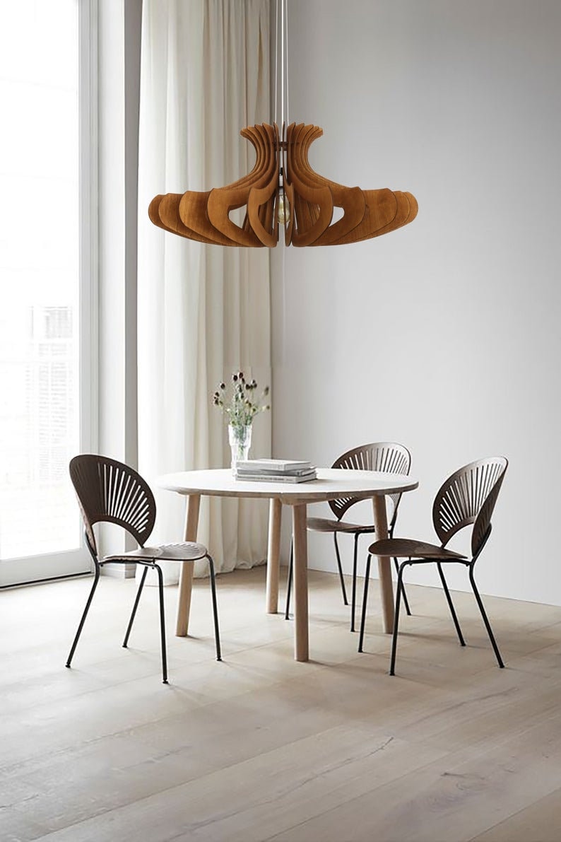 May include: A wooden dining table with four chairs. The table is round and has a light wood finish. The chairs are black metal with a brown woven seat. A wooden pendant light hangs above the table.