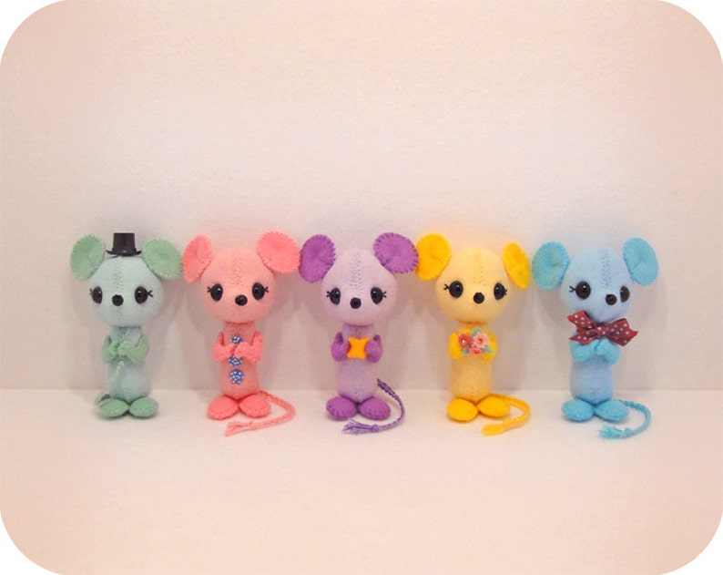 May include: Five felt mouse plushies in a row. The mice are light blue, pink, purple, yellow, and blue. Each mouse has a different design on its chest.