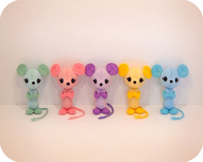 May include: Five felt mouse toys lined up. The mice are light blue, pink, purple, yellow, and blue. Each mouse has a small, black nose and black eyes. The mice are all standing upright with their arms crossed.