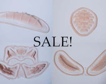 May include: Four prosthetic makeup pieces in various shapes and sizes, with a flesh-toned colour and a white border. The word "SALE!" is displayed in black, bold text.