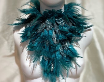 May include: Teal feather collar with a silver mesh design. The collar is displayed on a white mannequin bust. The text "Dellton Couture" is visible in the bottom right corner of the image.