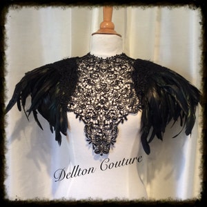 May include: Black lace collar with black feather shoulder pieces. The collar is a delicate lace design and the feathers are soft and fluffy. The collar is on a white mannequin. The text "Dellton Couture" is printed on the mannequin's chest.