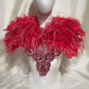 May include: A red feather boa with a red lace collar. The boa is worn on a white mannequin. The text "Dellton Couture" is visible in the bottom right corner of the image.