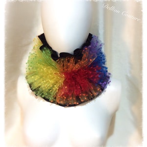 May include: Rainbow tulle collar with polka dots. The collar is made of multiple layers of tulle in a rainbow of colors, with small white polka dots on each layer. The collar is gathered at the center, creating a ruffled effect.