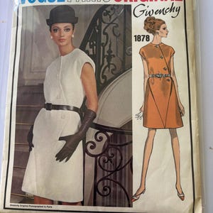 May include: A Vogue Paris Original Givenchy sewing pattern envelope, number 1878. The front features a photograph of a white sleeveless dress with a dark belt and gloves, alongside an illustration of an orange dress with a jeweled belt.