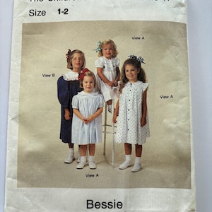 May include: The Children's Corner Patterns 11, Size 1-2, Bessie. A sewing pattern envelope featuring four children wearing various dresses labeled View A and View B. The dresses include a dark blue long-sleeve dress, a white dress, and a white dress with blue dots.