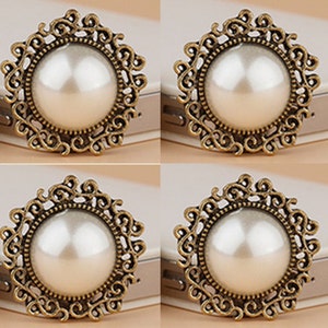 May include: Four gold-toned metal embellishments with a pearl center. Each embellishment features a decorative, ornate design.