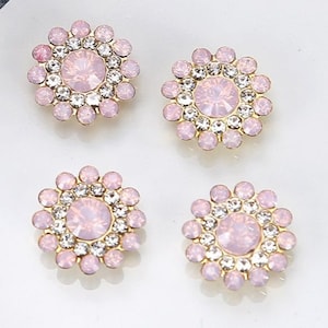 Può includere: Quattro decorazioni in strass rosa e oro con un grande strass rosa al centro di ciascuna.