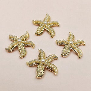 Può includere: Quattro decorazioni a forma di stella marina dorate con accenti di perle. Ogni stella marina ha una perla al centro ed è circondata da perle più piccole.