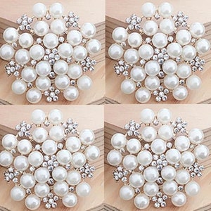 May include: Four white pearl brooches with silver accents. Each brooch is a snowflake design with a cluster of pearls in the center.
