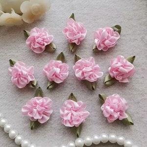 Pode incluir: Dez flores de tecido rosa com folhas verdes. As flores são feitas de fita e têm um aspecto enrugado.