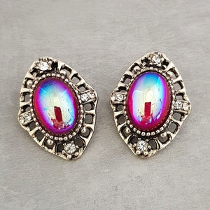 Op de afbeelding: Een paar zilveren oorbellen met iriserende roze ovale stenen, gezet in sierlijke frames met heldere strass.