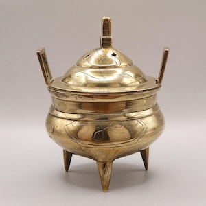 Op de afbeelding: Een gouden metalen wierookbrander met een deksel en drie poten. De brander heeft ingewikkelde bloemmotieven.