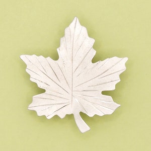 May include: A silver maple leaf brooch with a detailed, textured design.
