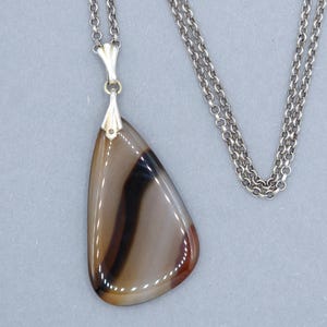 Op de afbeelding: Een zilveren ketting met een hanger van bruin en wit agaat. De hanger heeft een traanvorm met een zilveren lus.