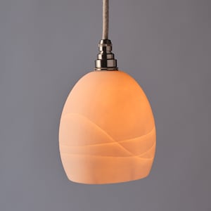 Puede incluir: Una lámpara colgante de cerámica blanca con un diseño ondulado. La luz cuelga de un cable y tiene un acabado de níquel.