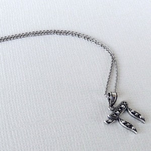 Puede incluir: Un collar de cadena de plata con un colgante de plata en forma de la letra hebrea Jai. El colgante está decorado con pequeñas cuentas.