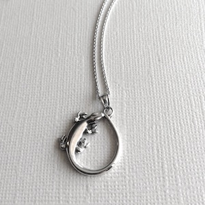 May include: A silver necklace with a pendant shaped like a lizard curled into a circle.