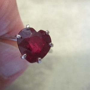 May include: A silver ring featuring a heart-shaped, deep red gemstone. The gemstone is held in place by four prongs. The date "08/04/2024" is visible in the background.