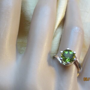 May include: A silver ring with a green gemstone set in a prong setting. The ring has a twisted band.