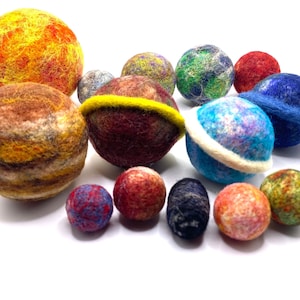 May include: A set of felt planets in various colors and sizes, including red, orange, yellow, blue, green, and brown. The planets are arranged in a semi-circle on a white background.