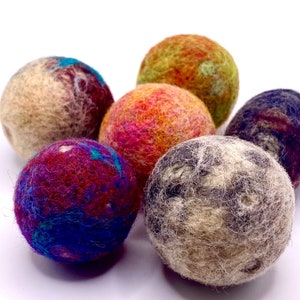 May include: A collection of six colorful felt balls. The balls display a variety of colors, including red, blue, orange, green, and brown. The felt balls have a textured, woolly appearance.