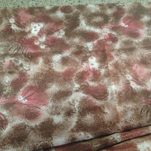 May include: A brown and pink fabric with a floral pattern. The fabric has a speckled texture and features a repeating pattern of pink flowers with white centers and brown stems.