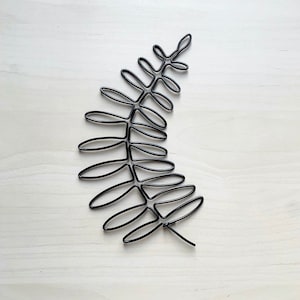 May include: Black metal fern leaf wall decor. The leaf is made of wire and has a simple, modern design.