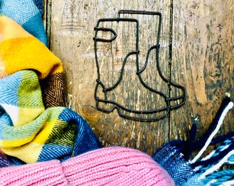 May include: A wire sculpture of two black wellies on a wooden background. The boots are in a simple, minimalist style.