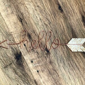 May include: A copper wire arrow with a glitter arrowhead and the word "hello" written in cursive.