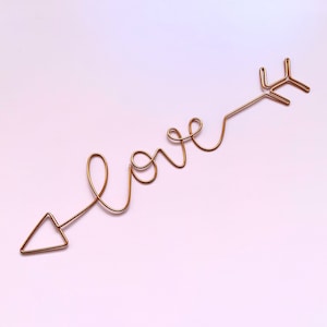 May include: A gold wire sculpture of an arrow with the word "love" written in cursive along the shaft.