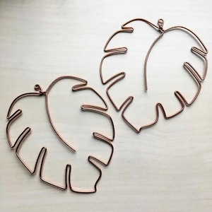 May include: Two copper wire sculptures of monstera leaves. The leaves are made of thin wire and have a delicate, airy look.