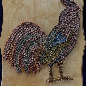 May include: A rooster made of metal tacks on a wooden background. The rooster is made of silver, gold, and copper tacks. The rooster is standing on a wooden surface.