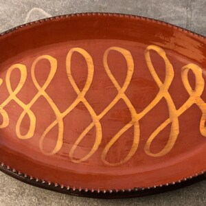 May include: An oval terracotta serving platter with a decorative design of a yellow, wavy pattern.