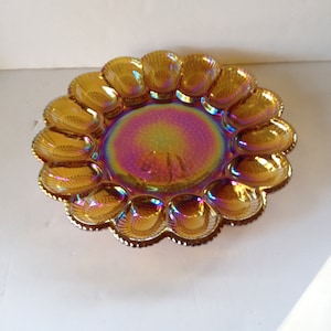 May include: A vintage amber iridescent glass egg plate with 12 individual compartments. The plate has a scalloped edge and a shiny, iridescent finish.
