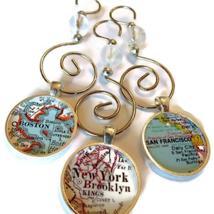 May include: Three gold-colored metal ornaments with glass beads and map-themed charms. The charms feature vintage maps of Boston, New York, and San Francisco.