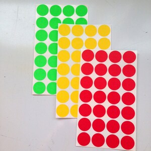 Puede incluir: Tres hojas de pegatinas redondas en colores brillantes: verde, amarillo y rojo. Cada hoja tiene una cuadrícula de círculos espaciados uniformemente. Las pegatinas están sobre un fondo blanco.