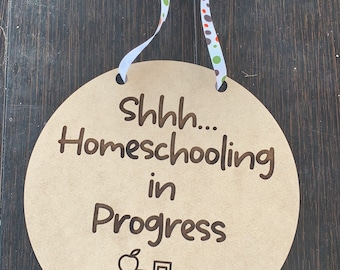 May include: A round wooden sign with the text "Shhh... Homeschooling in Progress" and a drawing of a stack of books with an apple on top.