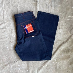 May include: A pair of dark blue denim jeans with orange stitching. The jeans have a Workmaster label with the text "Highest Quality" and "Size 38" on it.