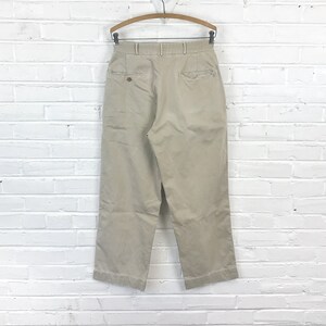 May include: Beige high-waisted pants with a pleated front and a button closure. The pants have a relaxed fit and a straight leg.