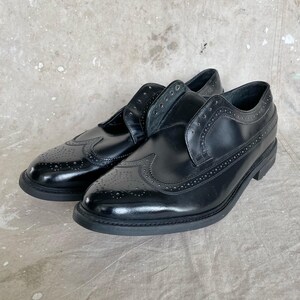 May include: A pair of black leather dress shoes with brogue detailing. The shoes have a classic wingtip design with decorative perforations and a rounded toe. The soles are black and the shoes appear unworn.