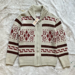 May include: A beige zip-up cardigan with a shawl collar and geometric patterns in maroon. The sweater features a full zipper and a tag attached to the collar. The design includes horizontal and vertical bands.