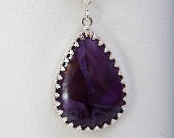 May include: A silver chain necklace with a teardrop-shaped pendant featuring a purple gemstone with a swirling pattern.