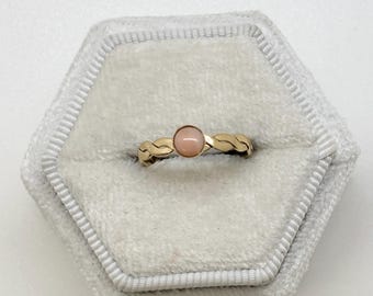 May include: A gold ring with a braided band and a pink gemstone.