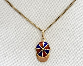 Puede incluir: Collar dorado con un colgante en forma de gorra de béisbol. La gorra está esmaltada en rojo, azul y dorado, con una visera dorada. La cadena es de tipo eslabón.