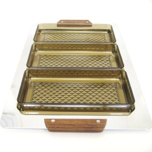 Puede incluir: Una bandeja rectangular con tres fuentes de vidrio color &aacute;mbar. Las fuentes tienen un patr&oacute;n de diamantes y se colocan sobre una bandeja plateada. La bandeja tiene asas de madera. Un juego de servir vintage.