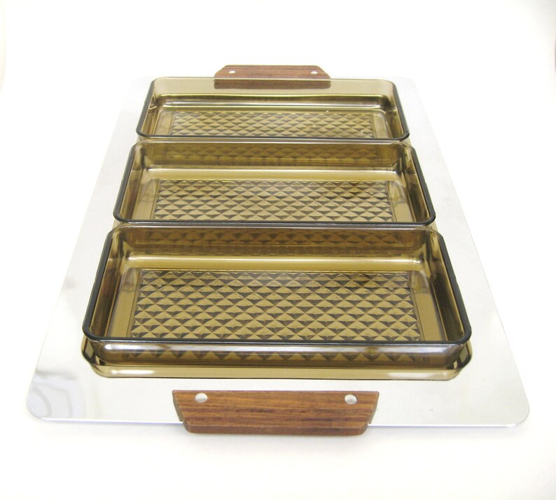 Puede incluir: Una bandeja rectangular con tres fuentes de vidrio color &aacute;mbar. Las fuentes tienen un patr&oacute;n de diamantes y se colocan sobre una bandeja plateada. La bandeja tiene asas de madera. Un juego de servir vintage.
